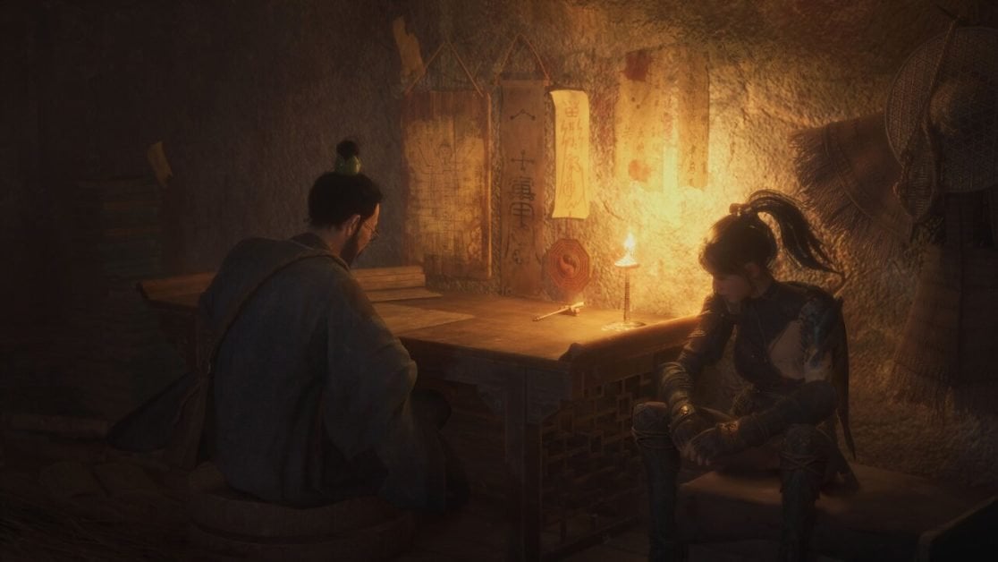 Two characters sit and talk by candlelight in a room