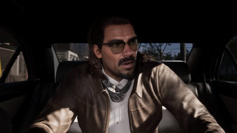 Bespectacled man speaks from the back seat of a car during daylight