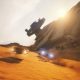 Two racing vehicles speed across orange desert sand beside a massive wrecked starship in Star Wars: Galactic Racer.