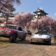Performance cars drive past cherry blossom trees with a Japanese castle in the distance.