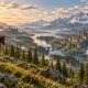 A traveler on horseback overlooks a river valley, pine forests, a settlement and distant snowy mountains.