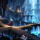 A small masked adventurer stands among branching passages and glowing pools in a ruined underground sanctuary.