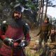 Medieval travelers stand beside a horse in a wooded landscape in Kingdom Come: Deliverance II.