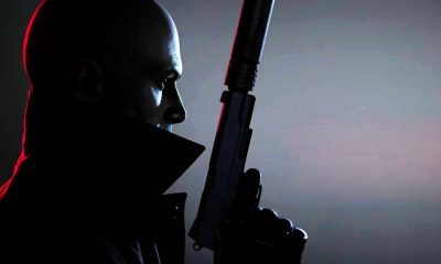 Agent 47 holds a suppressed pistol in a dark cinematic portrait with red rim lighting.