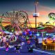 Blocky Roblox characters explore a theme park with colorful rides and roller coasters at sunset.
