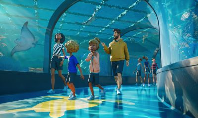 Visitors walk through a blue-lit aquarium viewing tunnel in Planet Zoo 2.