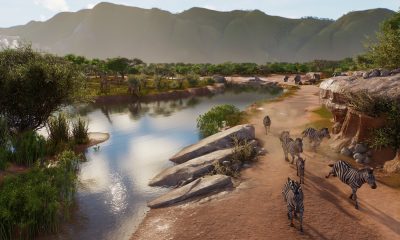 Visitors follow a path beside a river and a zebra habitat in Planet Zoo 2.