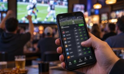 Hand holding a phone showing a sportsbook odds screen in a sports bar