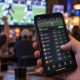 Hand holding a phone showing a sportsbook odds screen in a sports bar