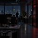 Dark game-studio office at night with a server room glowing red behind glass